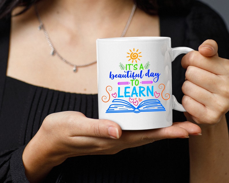 May include: White ceramic mug with a colorful design that says "It's a beautiful day to learn" with a sun, book, and hearts.