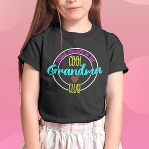 May include: A black t-shirt with a white circle and the text "Proud Member of the Cool Grandma Club" in colorful letters. A small heart with glitter is inside the circle.