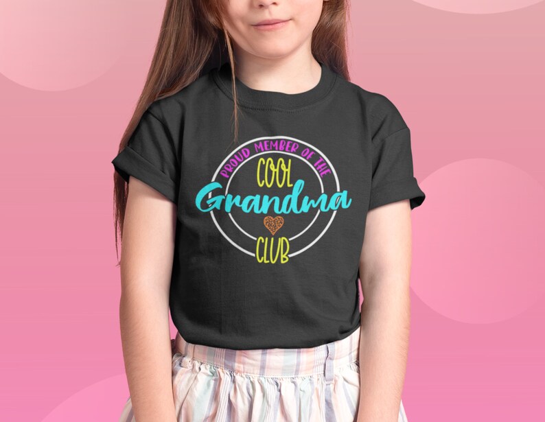May include: A black t-shirt with a white circle and the text "Proud Member of the Cool Grandma Club" in colorful letters. A small heart with glitter is inside the circle.
