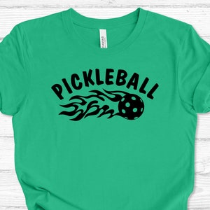 May include: A green t-shirt with a black graphic of a pickleball with flames and the text "Pickleball".