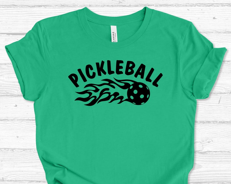 May include: A green t-shirt with a black graphic of a pickleball with flames and the text "Pickleball".