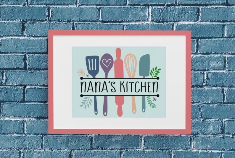 May include: A framed print with a light blue background featuring a spatula, spoon, rolling pin, whisk, and a spatula with a heart design. The text "NANA'S KITCHEN" is printed in black below the kitchen utensils.