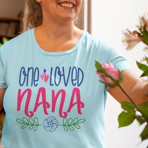 May include: A light blue t-shirt with the text "one loved nana" in pink and blue lettering. The shirt has a floral design with green leaves and a blue flower.