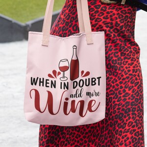 May include: Pink tote bag with a red wine glass and bottle graphic. The text reads "When in doubt add more wine".