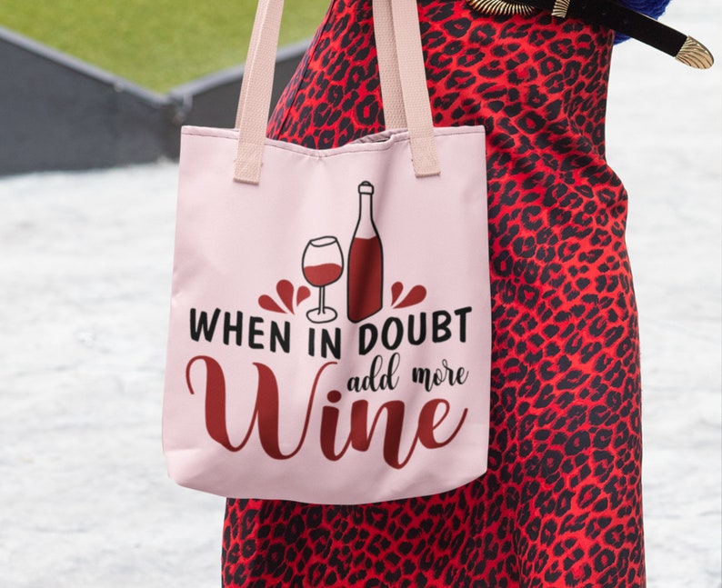 May include: Pink tote bag with a red wine glass and bottle graphic. The text reads "When in doubt add more wine".