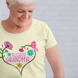 May include: A light yellow t-shirt with a pink ribbon, a heart-shaped floral design, and the text "Blessed Grandma".