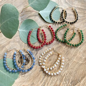 May include: Six pairs of gold hoop earrings with different colored beads. The earrings are made with red, green, blue, white, and black beads.