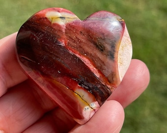 May include: Red, brown, and white heart-shaped polished stone with a layered pattern.