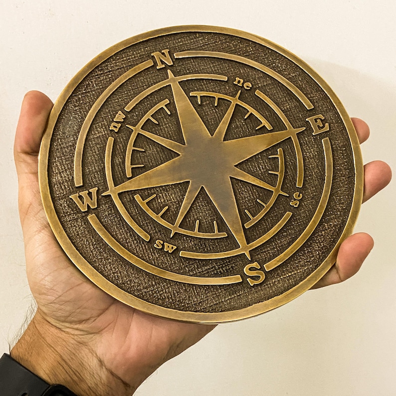 May include: A bronze-colored compass rose with directional markings (N, S, E, W, NE, SE, SW, NW) and a central star design. The compass is round and has a textured surface.