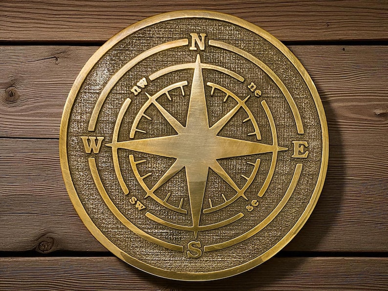 May include: A round, brass-colored compass rose with directional indicators (N, S, E, W, NE, NW, SE, SW) and a central star design. The compass is set against a textured background and mounted on a wooden surface.
