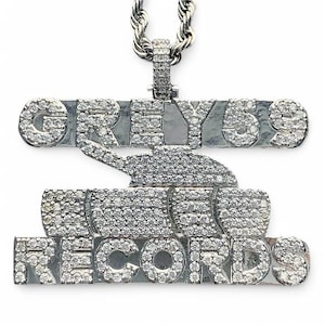 Może przedstawiać: Srebrny naszyjnik z zawieszką ozdobioną diamentami, przedstawiającą napis "GREY 59 RECORDS" i czołg.