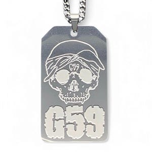 Op de afbeelding: Zilveren ketting met hanger met een schedel die een bandana draagt en het nummer "659" erop gegraveerd.