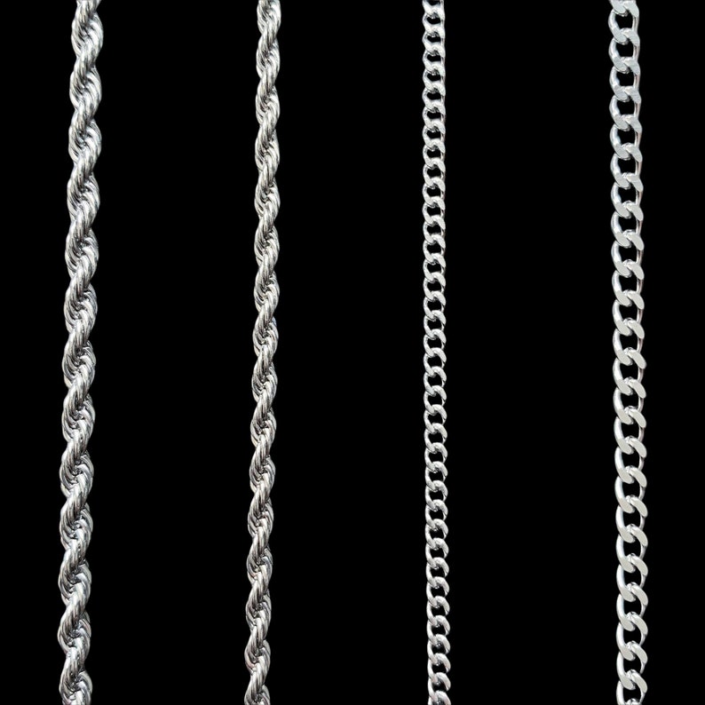 May include: Three silver chains of different styles hanging against a black background. The chains are all made of metal and have a shiny finish.