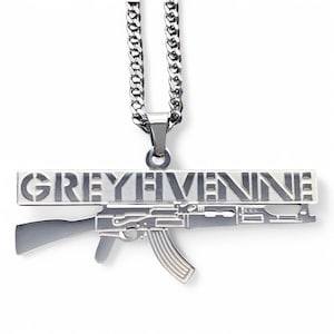 Op de afbeelding: Een zilveren ketting met een hanger met een gestileerd geweer met de woorden "GREY FIVE NINE" gegraveerd op een balk erboven.