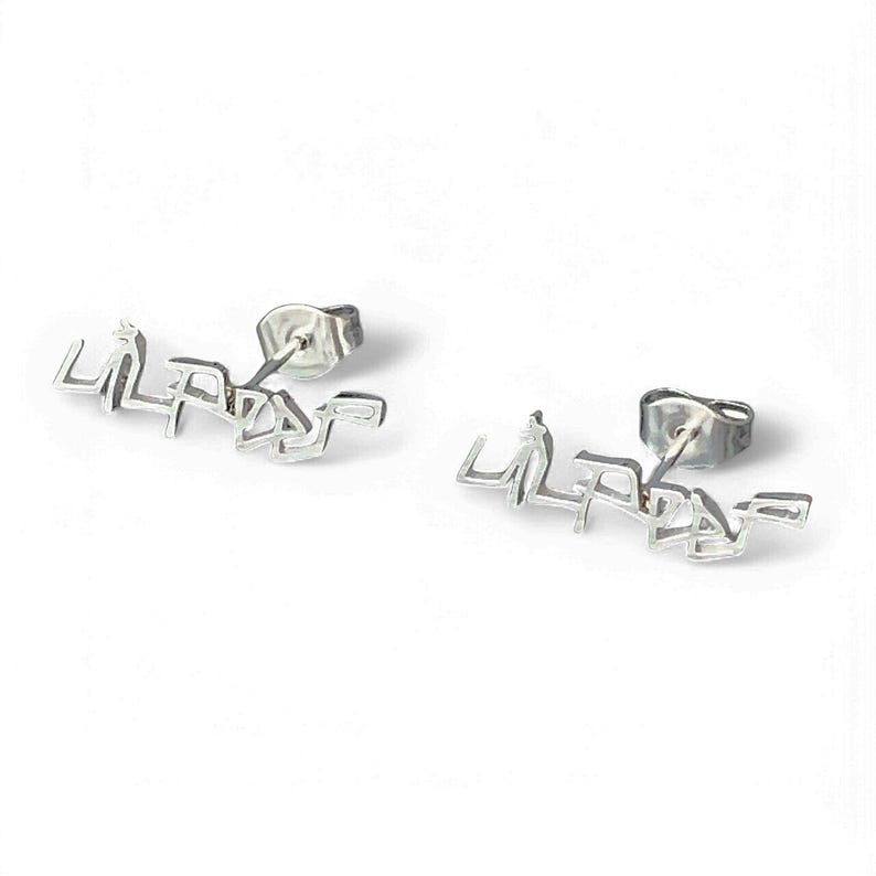 May include: A pair of silver earrings with the word "Lil Peep" spelled out in a stylized font.