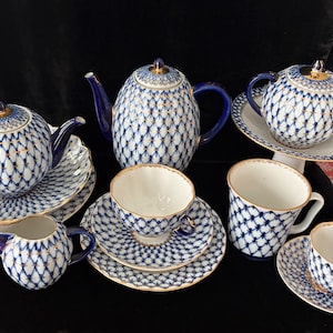 May include: A complete porcelain tea set featuring a blue and white lattice pattern with gold trim. The set includes a teapot, teacups, saucers, a creamer, and a sugar bowl. The tea set is arranged on a black surface.