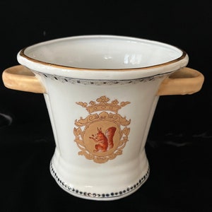 May include: White ceramic ice bucket with gold trim and a squirrel design. The bucket has two handles and a gold crown on the front.
