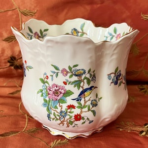 May include: A white ceramic planter with a scalloped rim and gold trim. The planter features a floral design with a blue bird perched on a branch.