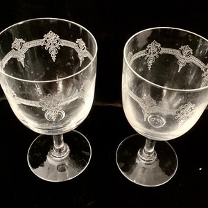 May include: Two clear glass wine glasses with etched floral designs around the top rim.