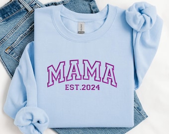 May include: Light blue sweatshirt with a purple embroidered design that says "MAMA EST. 2024".