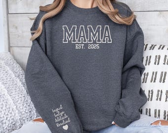May include: A dark gray sweatshirt with the text "MAMA EST. 2025" on the front. The sweatshirt has a white heart and the names Ingrid, Evelyn, Adelaide, and Rosalind on the left sleeve.
