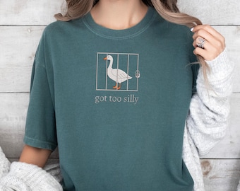 May include: Teal blue t-shirt with a white goose in a cage graphic and the text "got too silly".