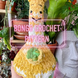 May include: A crocheted bongo drum in yellow and white with a green crocheted ball inside. The bongo drum is sitting on a hand and there are plants in the background. The text "BONGO CROCHET PATTERN" is written in pink on a white rectangle.