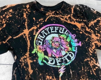 Könnte beinhalten: Schwarzes T-Shirt mit Batik-Effekt und einem kreisförmigen Aufdruck mit tanzenden Bären und den Worten "Grateful Dead". Die Grafik hat ein Regenbogenfarbschema. Das Shirt hat einen Rundhalsausschnitt und kurze Ärmel.