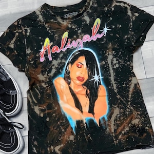 May include: Black t-shirt with a bleach-splattered design featuring a portrait of Selena with the text "Aaliyah" in pink, yellow, and blue lettering.