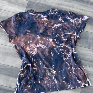 May include: A short-sleeved t-shirt with a unique tie-dye effect. The shirt features a dark navy blue base with brown and white splattered accents, creating a marbled appearance. The fabric appears soft and casual.