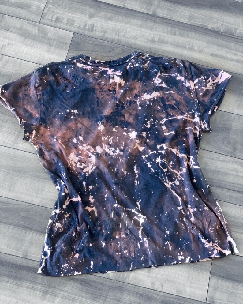 May include: A short-sleeved t-shirt with a unique tie-dye effect. The shirt features a dark navy blue base with brown and white splattered accents, creating a marbled appearance. The fabric appears soft and casual.