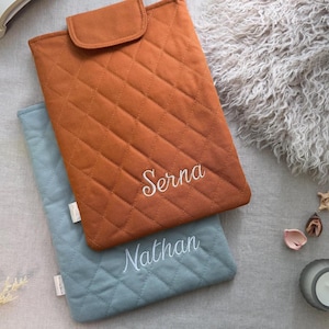 May include: Two rectangular quilted pouches with flap closures. The top pouch is rust orange with the name Serna embroidered in white script. The bottom pouch is dusty blue with the name Nathan embroidered in white script. Both feature diamond stitching.