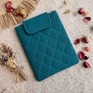 May include: A rectangular teal tablet sleeve featuring a quilted diamond pattern and a fold-over flap closure. The sleeve is constructed from a soft fabric material and displays a consistent stitched grid design across its entire front surface.