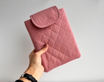 May include: A dusty rose quilted tablet case with a flap closure. The case has a diamond pattern and a textured surface. The flap is curved and matches the colour of the case.
