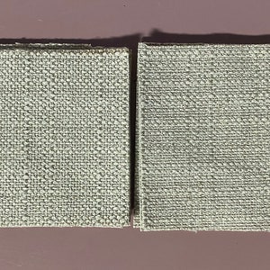 Op de afbeelding: Twee vierkanten van lichtgrijze geweven stof. De stof heeft een subtiele textuur en een licht ruw uiterlijk.