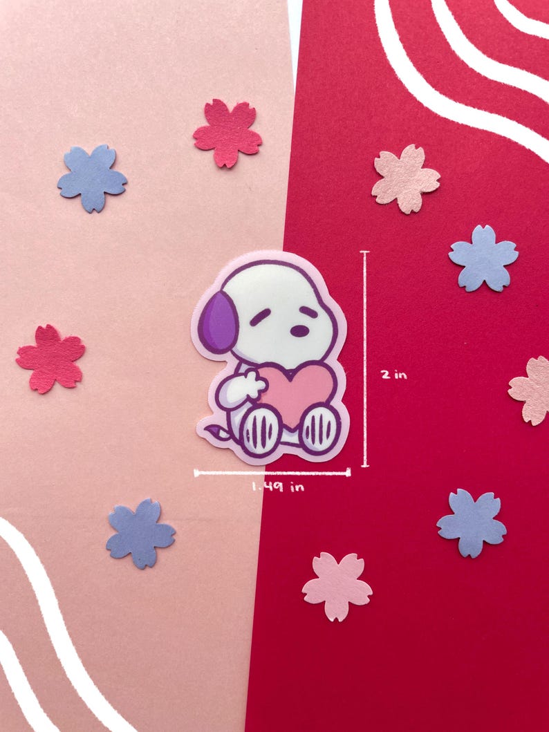 May include: A sticker featuring a cartoon dog with a purple ear and a pink heart. The sticker is 1.49 inches wide and 2 inches tall. The background is split between pink and red, with scattered flower-shaped cutouts in pink and blue.