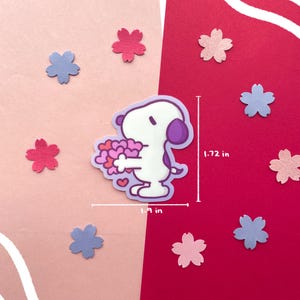 May include: A sticker featuring a cartoon character holding a bouquet of hearts, surrounded by pink and blue flower-shaped cutouts. The sticker is 1.9 inches wide and 1.72 inches tall. The background is split between pink and red.