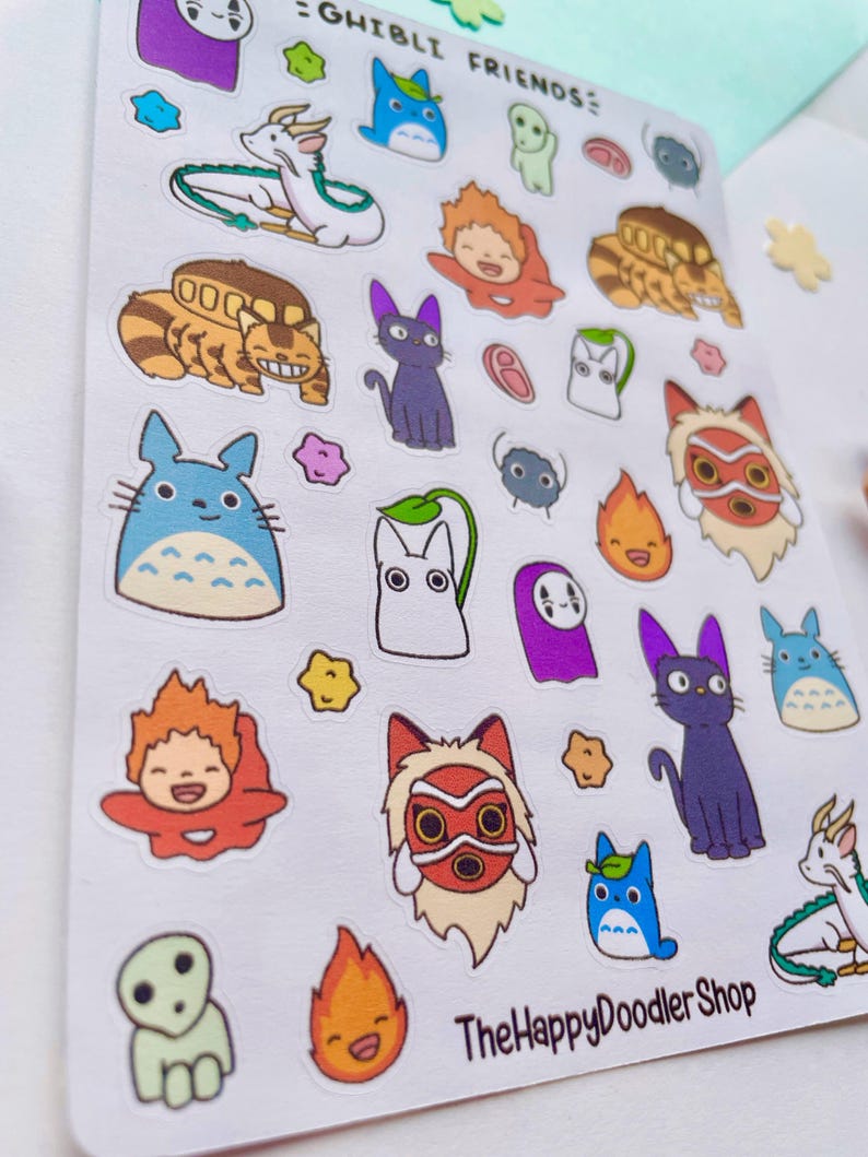 May include: A sheet of stickers featuring characters from Studio Ghibli films. The stickers are colorful and feature characters like Totoro, No Face, and Kiki's Delivery Service. The sheet is titled "Ghibli Friends" and includes the shop name "The Happy Doodler Shop".