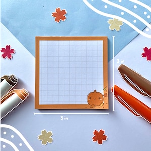 May include: A 3x3 inch orange and brown gridded notepad with a cute pumpkin illustration and autumn leaves. The notepad is on a light blue background with white and orange flower stickers.
