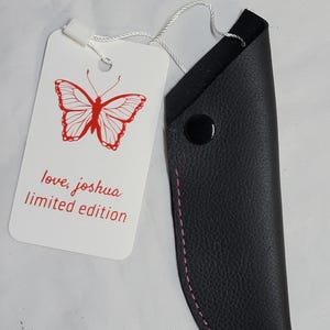 May include: Black leather sheath with pink stitching and a black snap closure. A white tag features a red butterfly illustration and the text "love, joshua limited edition".