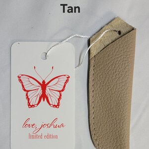 May include: A tan leather knife sheath with a white tag. The tag features a red butterfly design and the text "love, joshua limited edition". The word "Tan" is printed at the top.