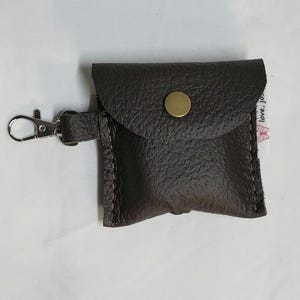 May include: A small, dark brown leather pouch with a snap closure and a metal clasp. The pouch has a textured surface and is stitched with a contrasting thread. The clasp is silver-colored.
