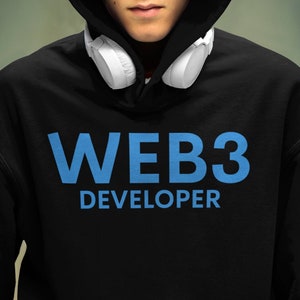 Può includere: Una persona indossa una felpa con cappuccio nera con il testo "WEB3 DEVELOPER" in lettere blu. La persona indossa delle cuffie bianche intorno al collo.