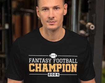 Può includere: Maglietta nera con una grafica dorata che dice "Fantasy Football Champion 2024" e un'icona di football.