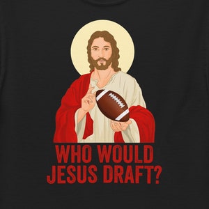May include: Black t-shirt featuring an illustration of Jesus holding a football, with a halo. The text "WHO WOULD JESUS DRAFT?" is printed in red below the image. A humorous design for sports fans.