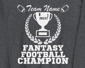 May include: Dark gray sweatshirt with white text and graphics. The design includes a trophy, footballs, and the words "Team Name," "2023," and "Fantasy Football Champion." A laurel wreath surrounds the trophy.
