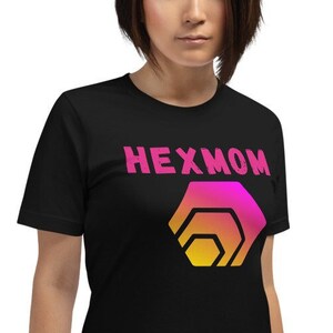 Puede incluir: Una camiseta negra con un diseño gráfico rosa y amarillo de un hexágono con el texto "HEXMOM" encima.