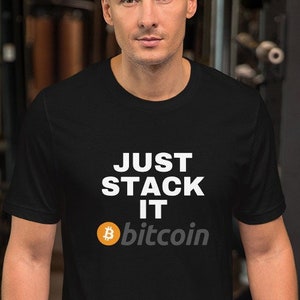 Puede incluir: Camiseta negra con el texto "JUST STACK IT" en blanco y el logotipo de Bitcoin con la palabra "bitcoin" debajo. La camiseta la lleva una persona en un gimnasio.
