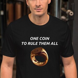 May include: Black t-shirt with white text that reads "ONE COIN TO RULE THEM ALL". A gold ring with a coin design is centered on the shirt.