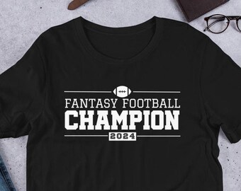 Può includere: Maglietta nera con testo bianco che dice "Fantasy Football Champion 2024" e un'icona di football.